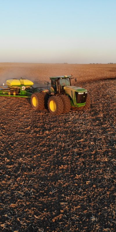 green tractor pulling a yellow fertilizer tank in a field.