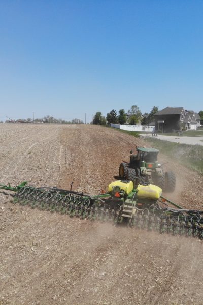 Green tractor pulling a sprayer though a farm field.